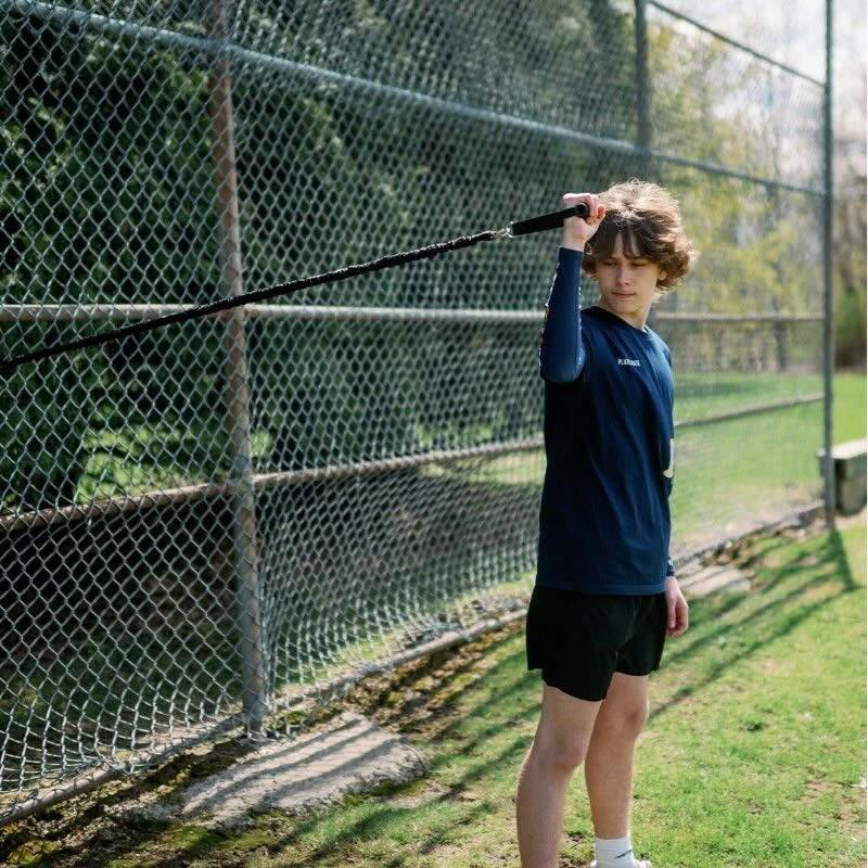 A young boy practices with the Plate Crate Pro Band in front of a chain-link fence.