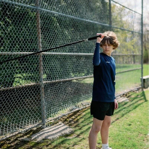 A young boy practices with the Plate Crate Pro Band in front of a chain-link fence.