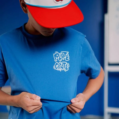A young boy wearing Plate Crate's Blue Doodle T-Shirt shows off the shirt's Plate Crate logo.